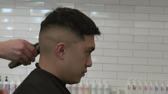 Stylist uses clippers to blend Asian customer's hair in the back