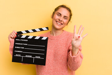 young pretty woman smiling and looking friendly, showing number four. cinema clapper concept