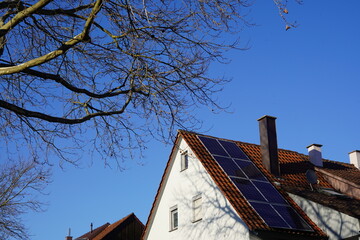 Photovoltaik Panele auf einem Wohnhausdach. Auch im Winter scheint die Sonne und der mächtige Baum wirft nur wenig Schatten auf das Dach