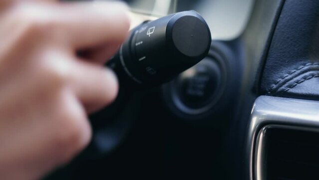 Hand of young business woman with red nails turn on and off lights switch in modern car close up. Person driver switches the lever.