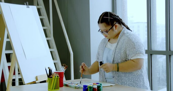 Asian Autistic girl wearing cute glasses mixing colors to draw on paper in room at home. Activities to enhance learning skill. Create imaginative ideas for children. Concept Education