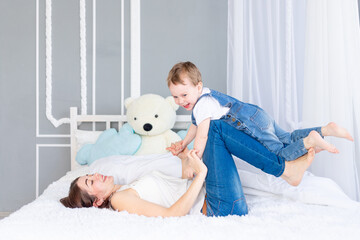 Obraz na płótnie Canvas A happy, loving family. Mom and baby son play at home on the bed, have fun and laugh