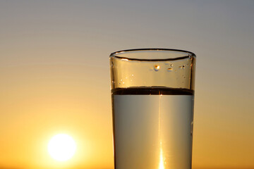 Clean water in drinking glass on sunset sky background. Concept of health and freshness, thirst,...