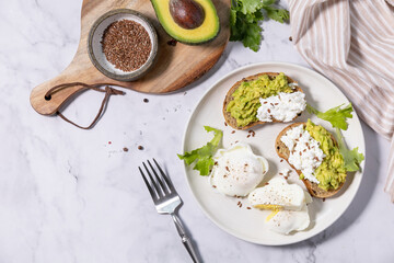 Easter breakfast or brunch. Delicious breakfast or snack - poached egg and cream cheese toast whole grain rye bread, avocado on a marble tabletop. Top view flat lay.