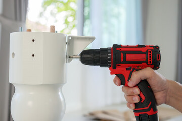 man assembling white table furniture at home using cordless screwdriver