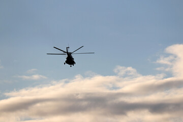 Fototapeta na wymiar Silhouette of military helicopter in flight in blue sky with clouds