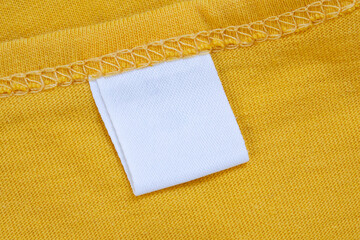 White blank clothing tag label on new yellow shirt background