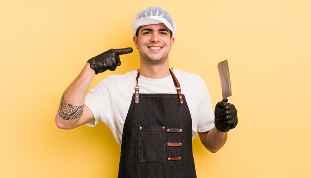young handsome man smiling confidently pointing to own broad smile. butcher concept