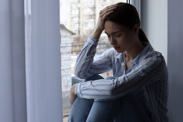 Fototapeta premium Unhappy young woman near window indoors, space for text. Loneliness concept