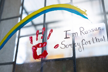 Picture on window with bars of Ucranian flag as a rainbow sign and a red handprint with an...
