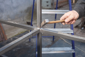 a man with a hammer beats scales when welding on an iron structure