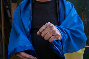 Stock photo old man tightly clutches the flag of his country Ukraine in the face of war with Russia. 