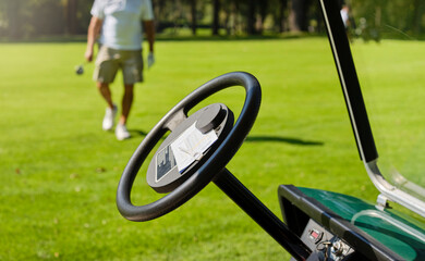 Fototapeta na wymiar The player keeps the score on the golf course. The score placed on the steering wheel of the golf car. In the background, a player with a club in hand prepares to drive the golf car.