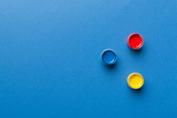 jars with gouache of different colors on Colored background. hobby painting. Top view with empty space. workplace for creativity. home teaching concept drawing