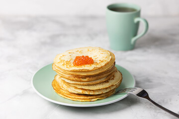 Pancakes for Maslenitsa with red caviar on a green plate. Pancakes in the hole. Selective focus.