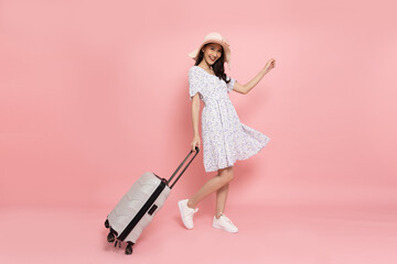 Happy young Asian woman traveler drag luggage isolated on pink background, Tourist girl having cheerful holiday trip concept, Full body composition