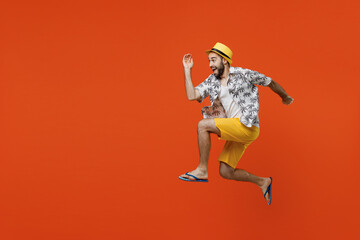 Full body side view fun excited young tourist man wear beach shirt hat jump high run fast hurry up isolated on plain orange color background studio portrait. Summer vacation sea rest sun tan concept.