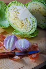 Fresh raw vegetables cut into two parts. Purple onion with peel and white cabbage on a wooden board, a small knife.