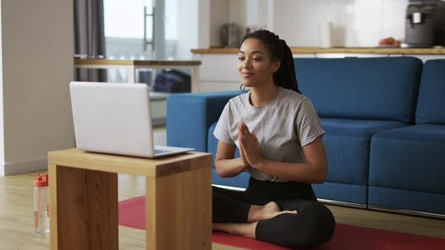 Young African woman doing yoga sitting in front the laptop