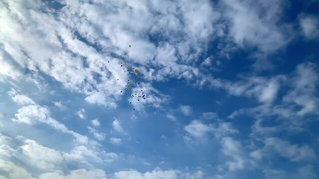 Balloons fly into the sky. Blue and yellow colors of the flag of Ukraine. Ukrainian support. Against the war. For peace. Flying balloons in the blue cloudy sky fly away. Freedom.