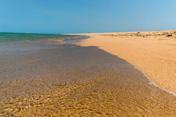 Fototapeta na wymiar Calmas ondas chegando em praia de areias escuras em ilha deserta, com mar ao fundo e céu azul, localizada em Cabrália, Bahia