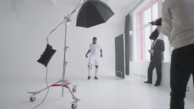 afro-american footballer is posing for camera of photographer in studio, showing kick-up skill