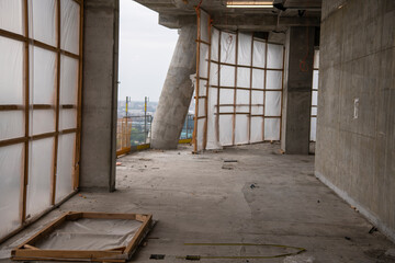 Empty floor of room or apartment of high-rise building skyscraper on construction site, unfinished, work in progress. Concrete pillars and walls. Construction and building materials and tools.