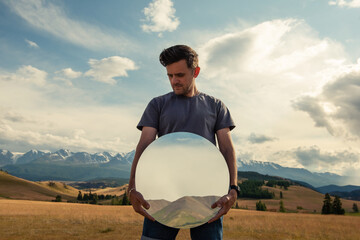 Man standing in in summer Altai mountains in Kurai steppe and holding circle mirror. Creative...