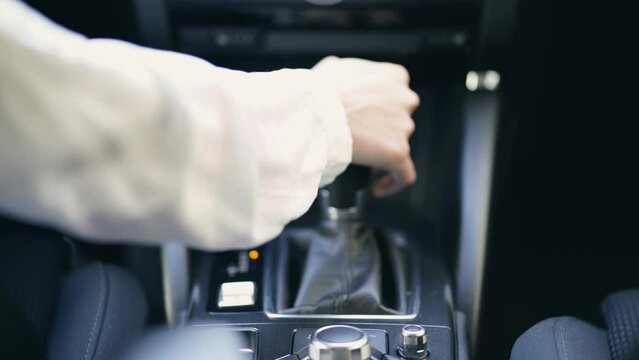Young woman changing speed by hand holding gearbox in car. Girl driver shifting gears. European female driving a car moving transmission shifting automatic transmission.