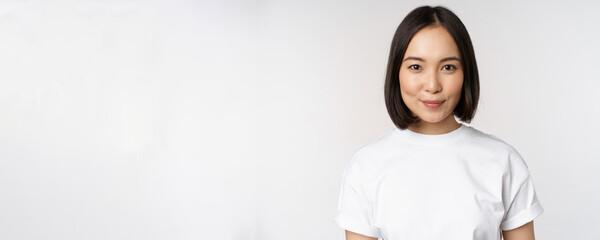 Close up portrait of young asian woman looking at camera, wearing t-shirt, smiling and looking...