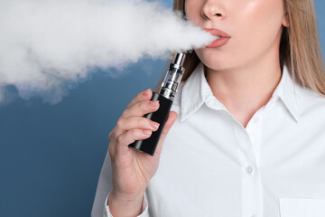Young woman using electronic cigarette on light blue background, closeup