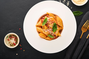 Bolognese Penne Pasta. Tasty appetizing classic italian penne pasta with parmesan, basil and Bolognese sauce in white plate on plate on black dark background.Traditional Italian cuisine. Top view.