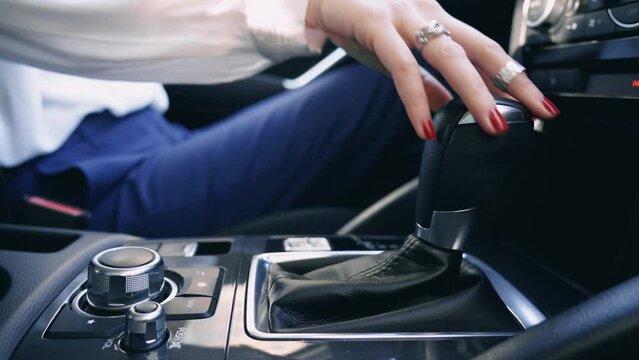 Businesswoman with red nails driving beautiful modern automatic car close up view. Automatic gear lever and gear shift. Inside