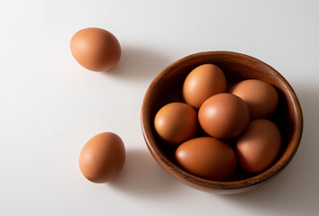 Top view brown eggs in wooden bowl on white table.