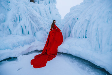 A girl in a red long dress with a train on the background of ice rocks. Girl in winter in the...