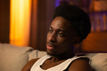 Close up portrait of a man with dark skin, beard and afro sitting on a couch, the boy wearing white...