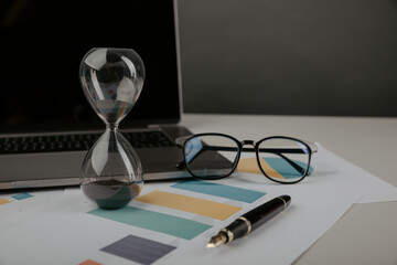 Hourglass on a workplace with reports. Time management concept