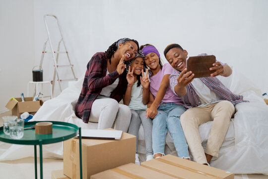 Cheerful family renovates a new apartment, laughing dad takes a selfie with his wife and kids, daughters fool around, pose for a photo, funny team