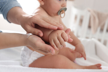 Mother massaging her baby with oil on changing table at home, closeup