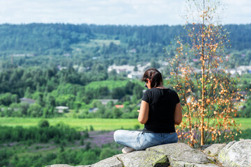 Young woman sits on the rocky surface of Mount Paasonvuori near the town of Sortavala in the Republic of Karelia.