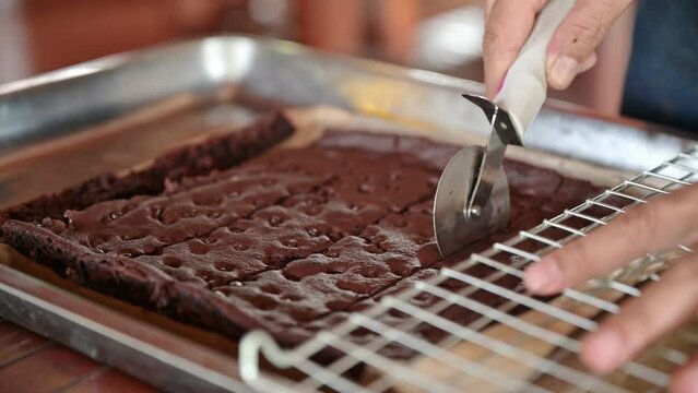 Baker hand using wheel cutter cutting on baked dark chocolate chip brownies in tray