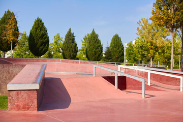 Pink skater ground in city park, with stunt rails, obstacles, ramp, slopes for active youthful people, trainings tricks and exercise, beautiful green tall funny wedge-shaped trees on background