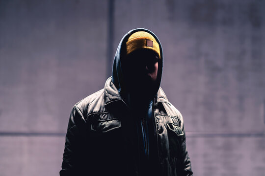Hooded criminal in dark. Mystery man with hood. Gangster in urban street. Hooligan in hoodie. Stalker with hidden face. Unknown suspicious thief, burglar, hacker or terrorist with grunge background.