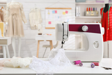 Modern sewing machine with fabric and bright threads on table in dressmaking workshop