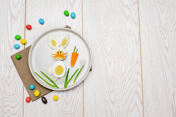 Easter Funny Creative Healthy breakfast lunch food idea for kids children.Bunny rabbit made from boiled eggs,peeled carrots, greens on plate white wood table background.Top view Flat lay, copy space