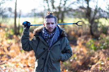 A portrait of a young bearded man with a litter picker ready to do a litter pick and clean up the...
