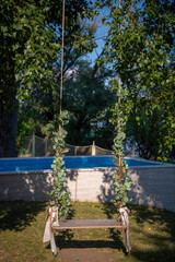 Romantic scene of a decorated swing hanging from tree branch by the pool in a lush garden.