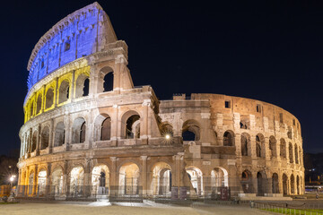 Naklejka premium Colosseum at night, Rome, Italy, lit with the yellow and blue colors of the Ukrainian flag.