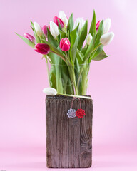 Martisor on a wooden backdrop in front of a transparent vase full with white and pink tulips