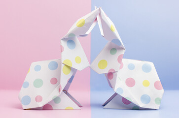 Two easter origami paper bunnies on pink and blue background